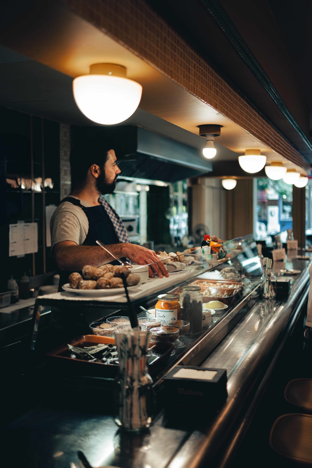 Ultramarinos Marín, Barcelona: a cook at the counter planxa with a tray of ceps