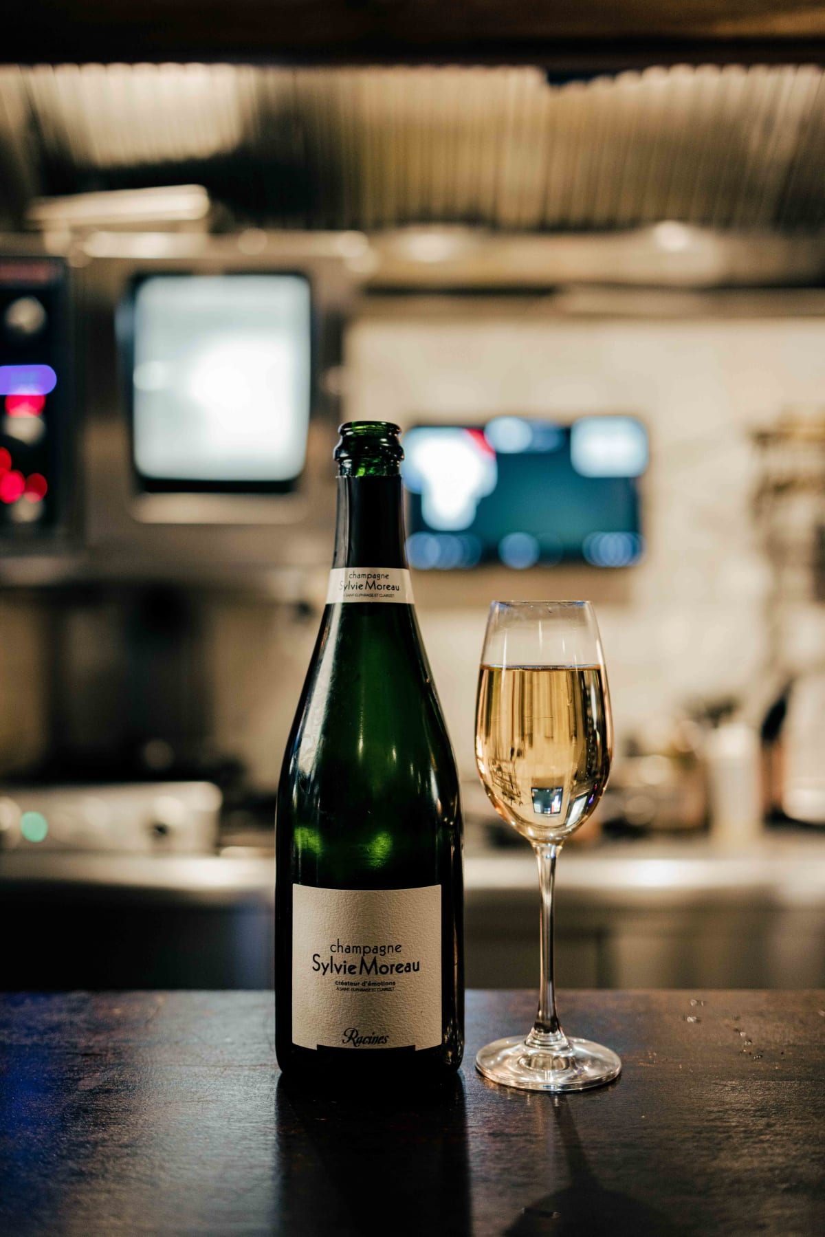 Bistro de la Mer, Amsterdam: a bottle of Champagne Sylvie Moreau Racines beside a poured glass, the kitchen behind