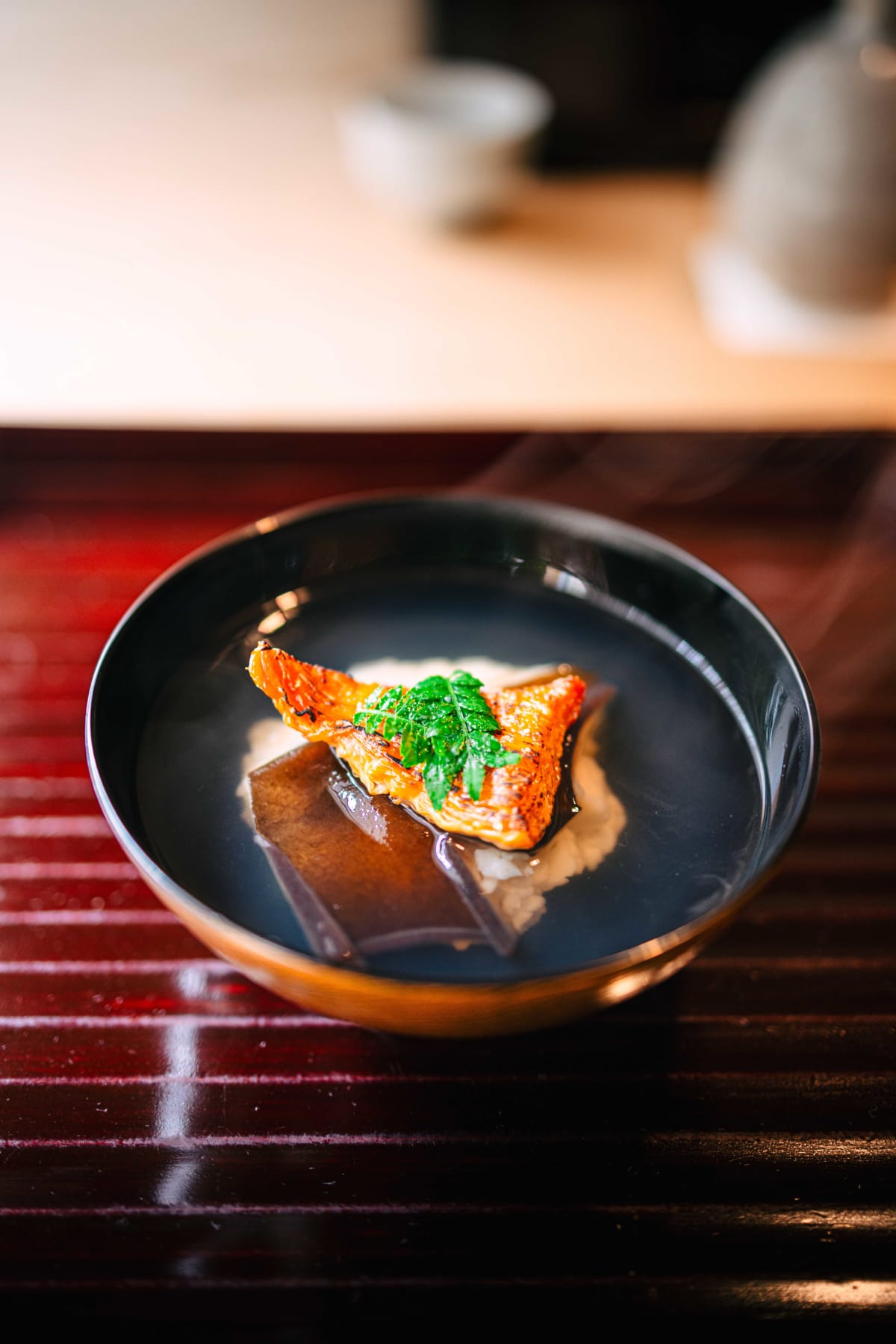 Matsukawa, Tokyo: the suimono in a black lacquer bowl, grilled bachiko and a sprig of kinome over the scallop