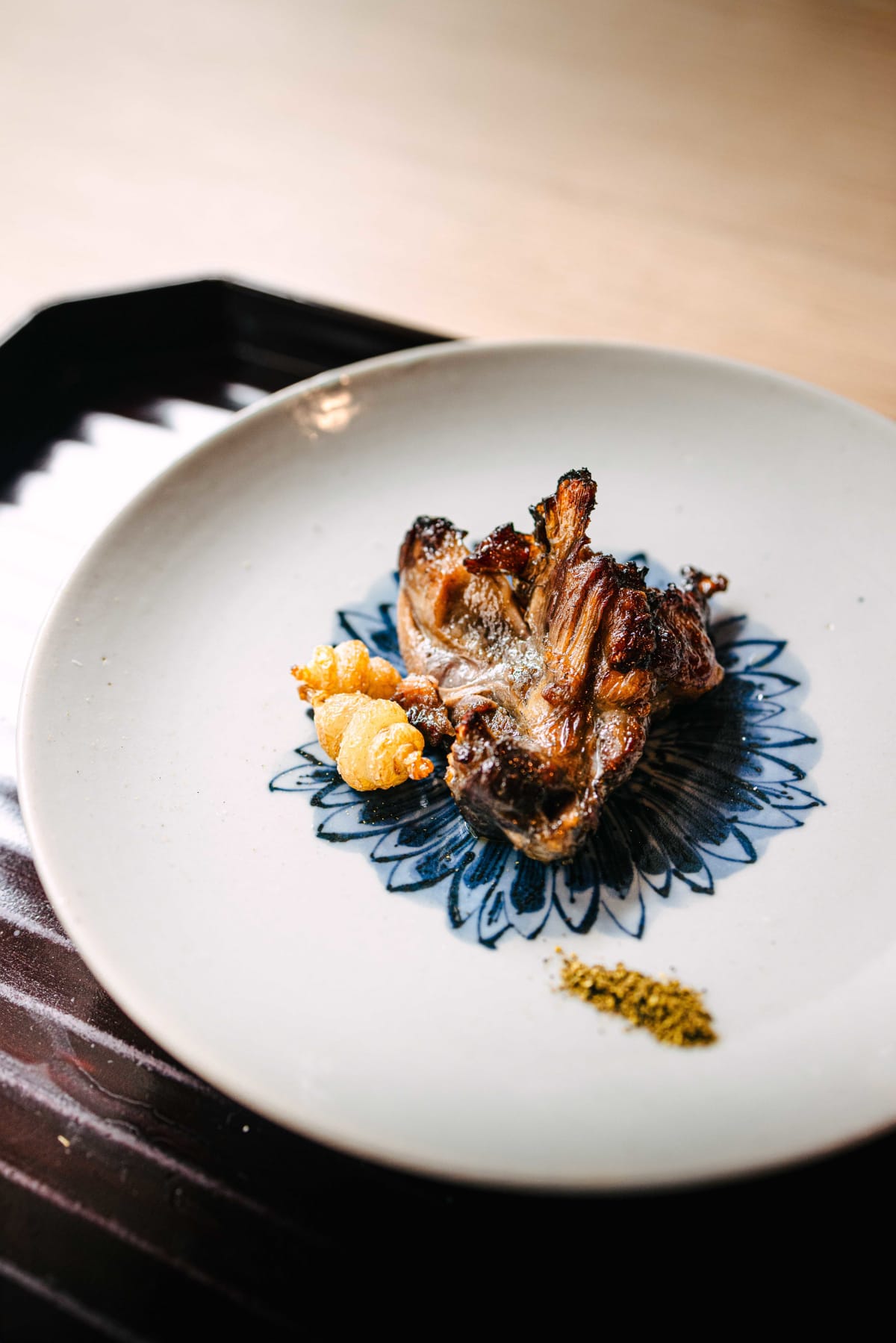 Matsukawa, Tokyo: soft-shelled turtle glazed with tare on a white plate painted with a blue chrysanthemum, sansho powder alongside