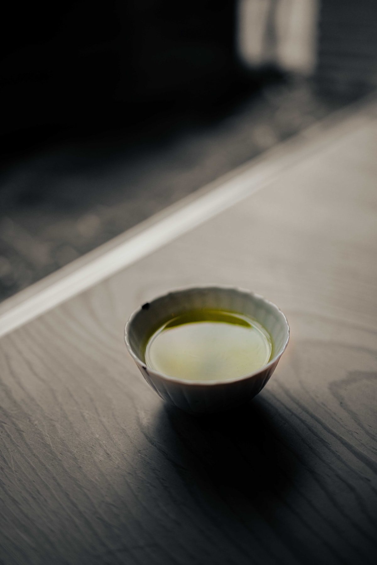 Matsukawa, Tokyo: a cup of green tea on a dark table, the room around it drained of colour