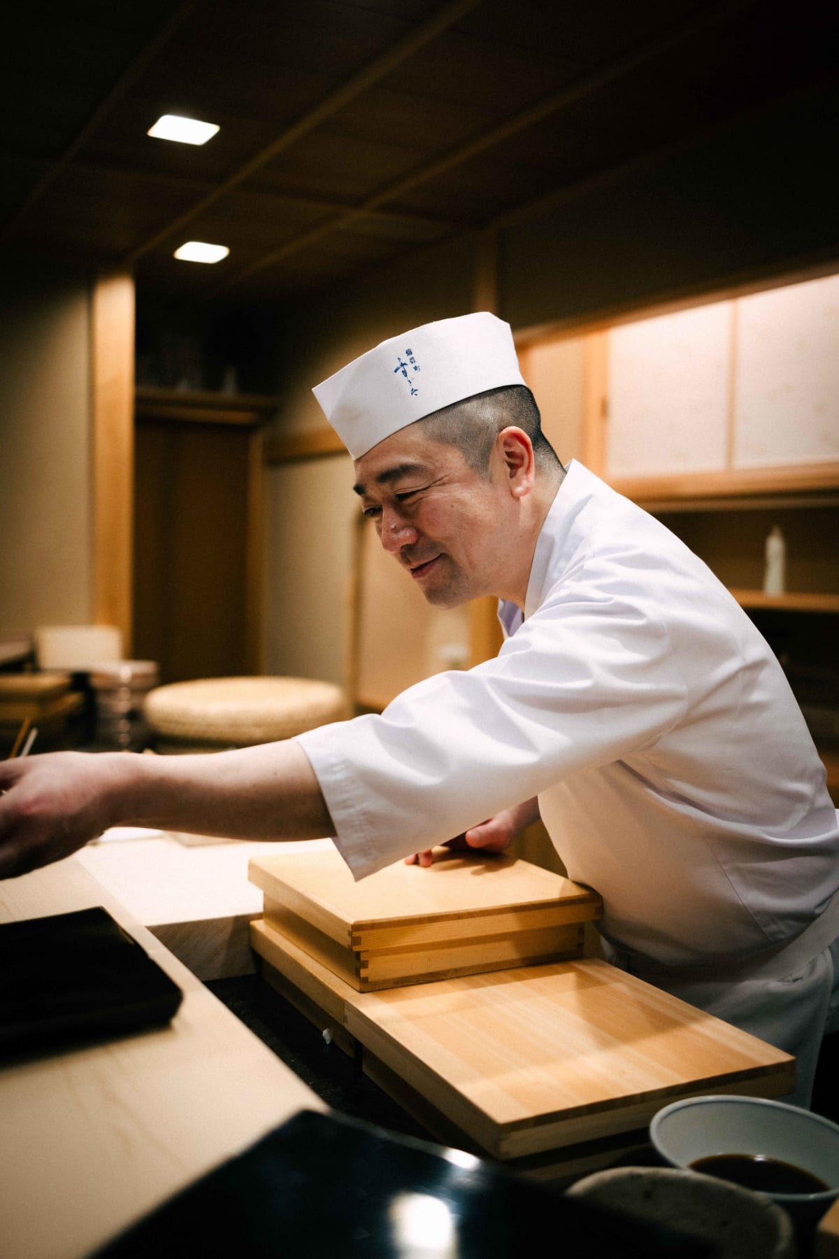 Nihonbashi Kakigaracho Sugita, Tokyo: Sugita handing the isobeyaki across the counter, smiling