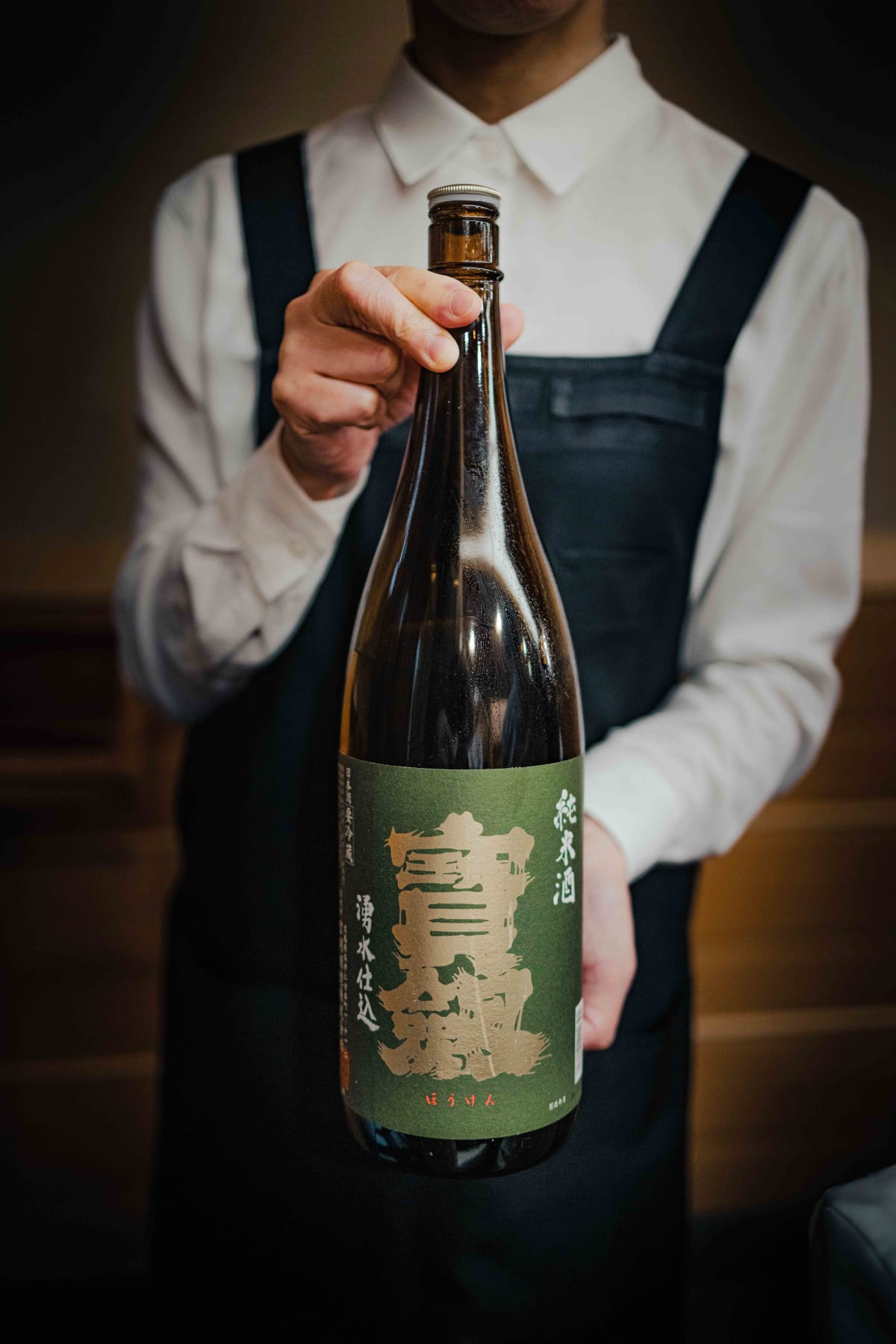 Nihonbashi Kakigaracho Sugita, Tokyo: a member of staff holding up the isshobin of Hoken junmaishu, 湧水仕込 on its green label