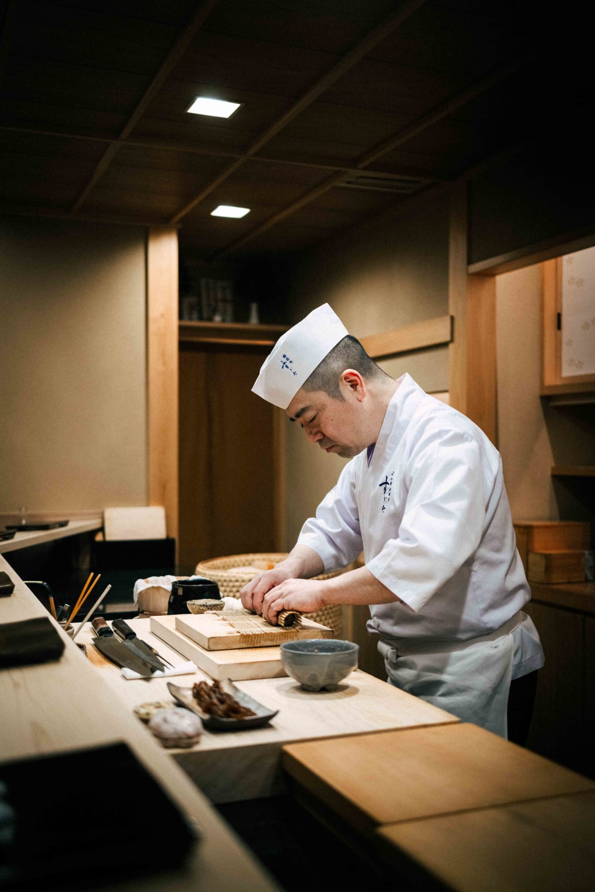Nihonbashi Kakigaracho Sugita, Tokyo: Sugita rolling a maki with a bamboo mat, the counter laid out before him