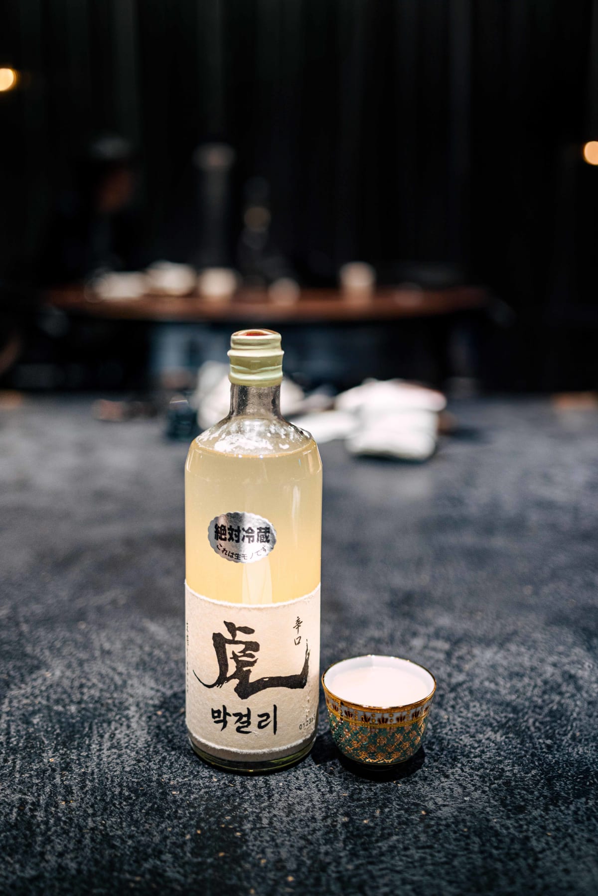 Florilège, Tokyo: Tora makgeolli, its label brushed with 虎 and 막걸리, beside a small gold-rimmed cup