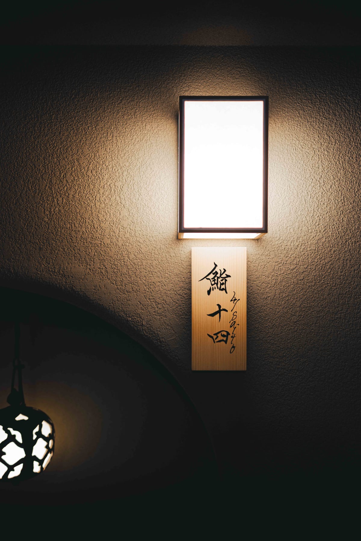 Sushi Juyon by Saito, Seoul: the wooden nameplate on the wall reading 鮨 十四 by saito, lit by a wall lamp