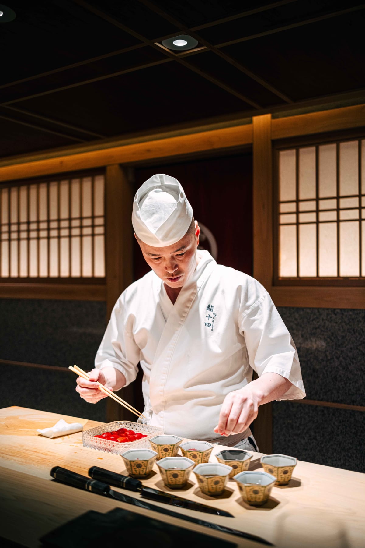 Sushi Juyon by Saito, Seoul: the taisho spooning mozuku into hexagonal dishes in the light that falls on his station