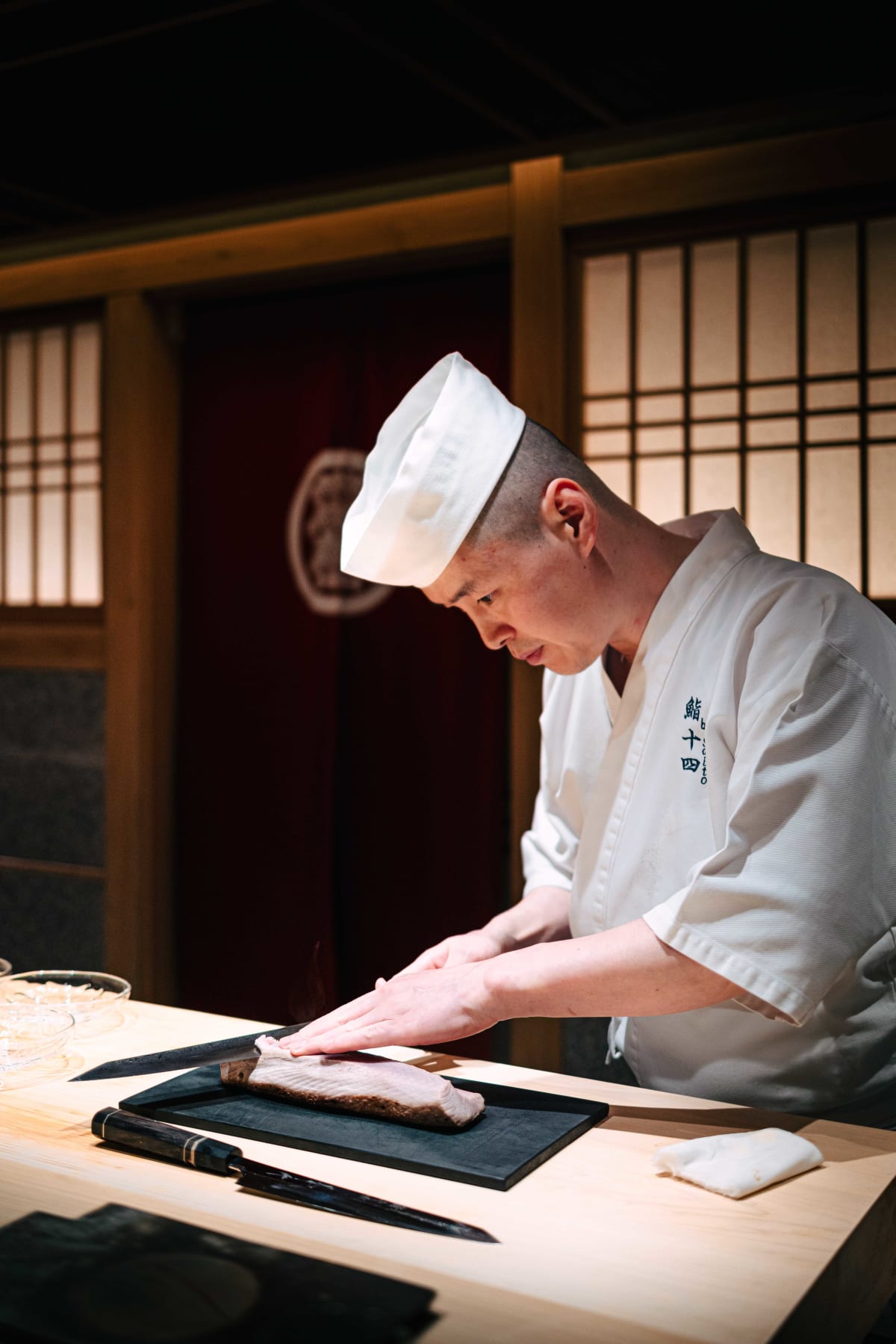Sushi Juyon by Saito, Seoul: the taisho trimming a seared block of meji maguro, slicing it and plating it on glass dishes