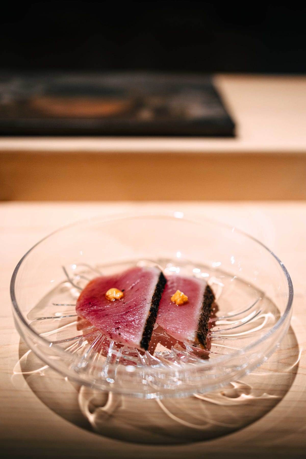 Sushi Juyon by Saito, Seoul: meji maguro, two pieces on a glass plate with blackened, seared surfaces and a dab of yellow condiment on each, then one lifted on chopsticks