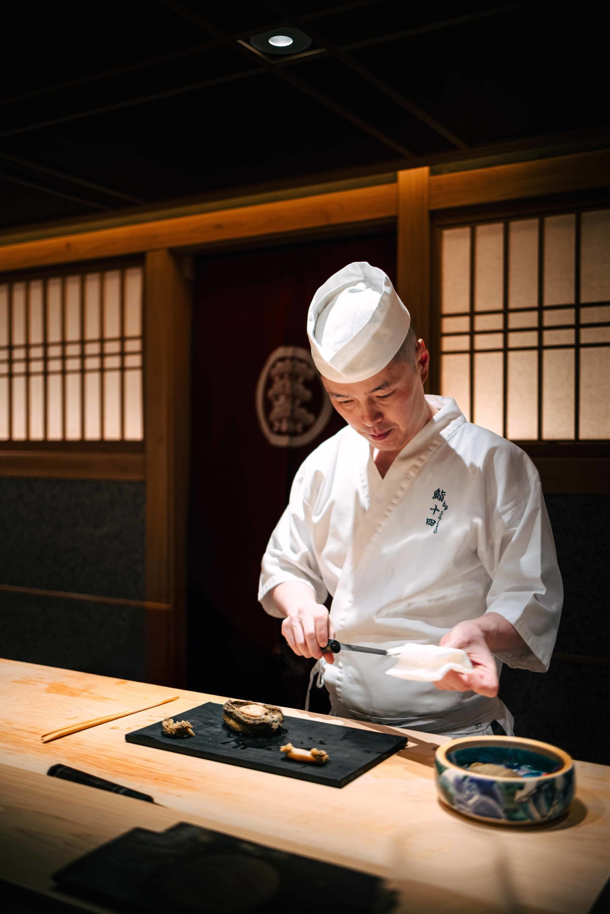 Sushi Juyon by Saito, Seoul: the taisho slicing a large steamed abalone, shako on the board and a bowl of liver sauce beside it