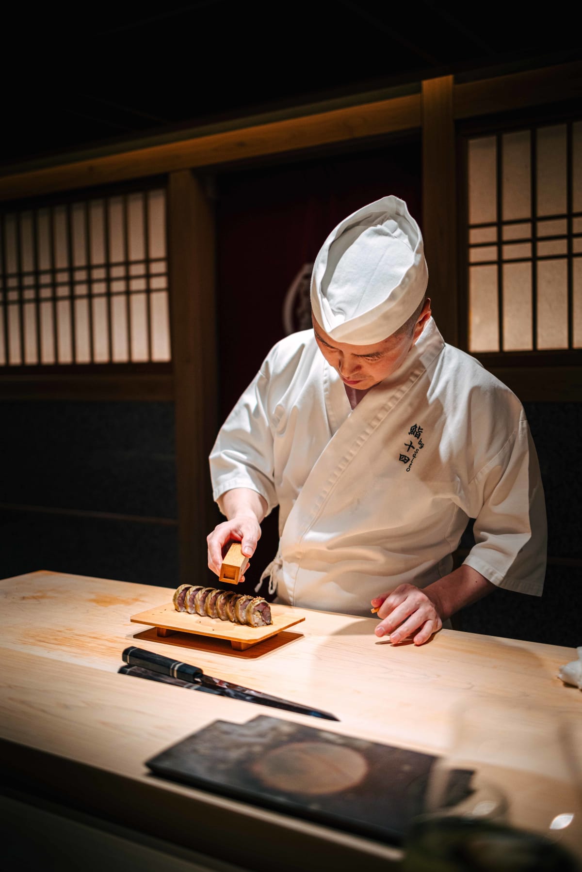 Sushi Juyon by Saito, Seoul: the taisho slicing the saba maki and dusting it with sesame from a wooden shaker, then handing over a piece wrapped in nori
