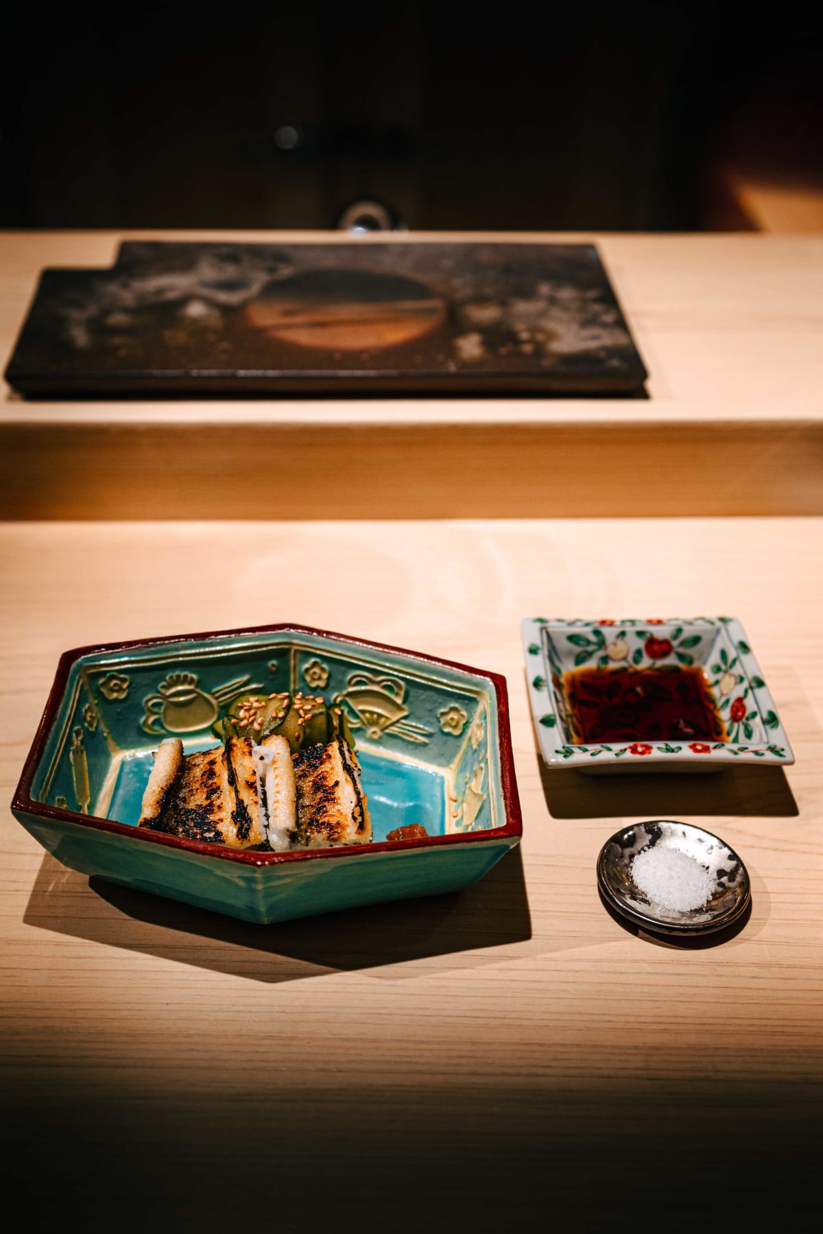 Sushi Juyon by Saito, Seoul: anago shirayaki in a teal hexagonal dish with pickled cucumber and sesame and an umeboshi, soy sauce and salt on the side