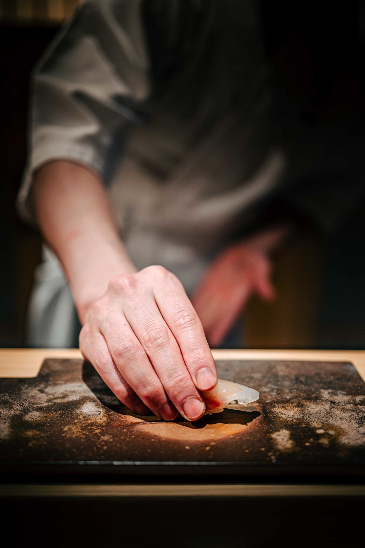 Sushi Juyon by Saito, Seoul: the taisho's hand setting a freshly formed nigiri on the geta