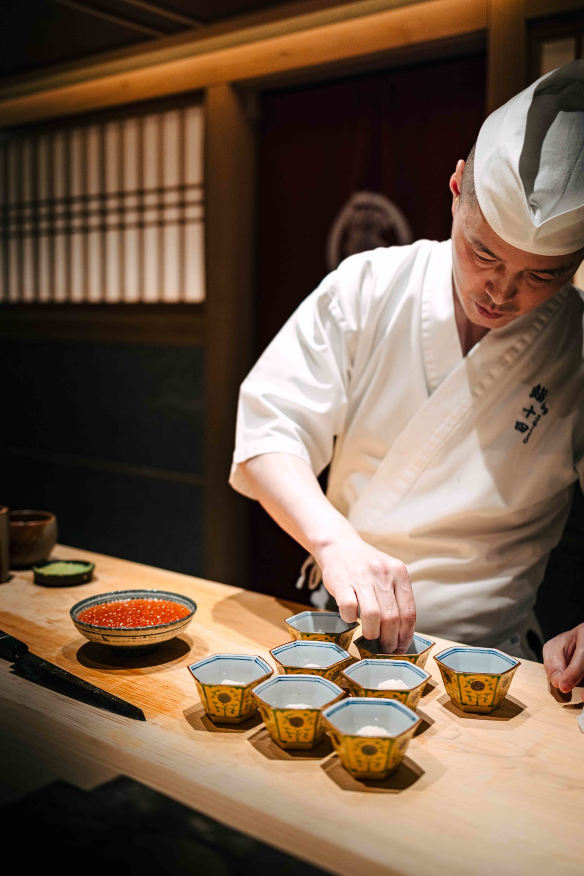 Sushi Juyon by Saito, Seoul: the taisho filling hexagonal dishes with shari, spooning the ikura over and finishing each with chopsticks