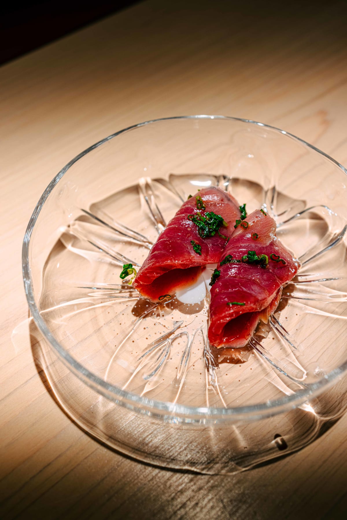 Sushi Juyon by Saito, Seoul: suma-gatsuo, two pieces rolled into rounds on a glass plate, scattered with chives around a white sauce