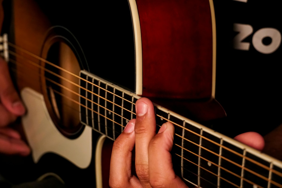 Close-up of hands playing acoustic guitar with visible fretboard and strings