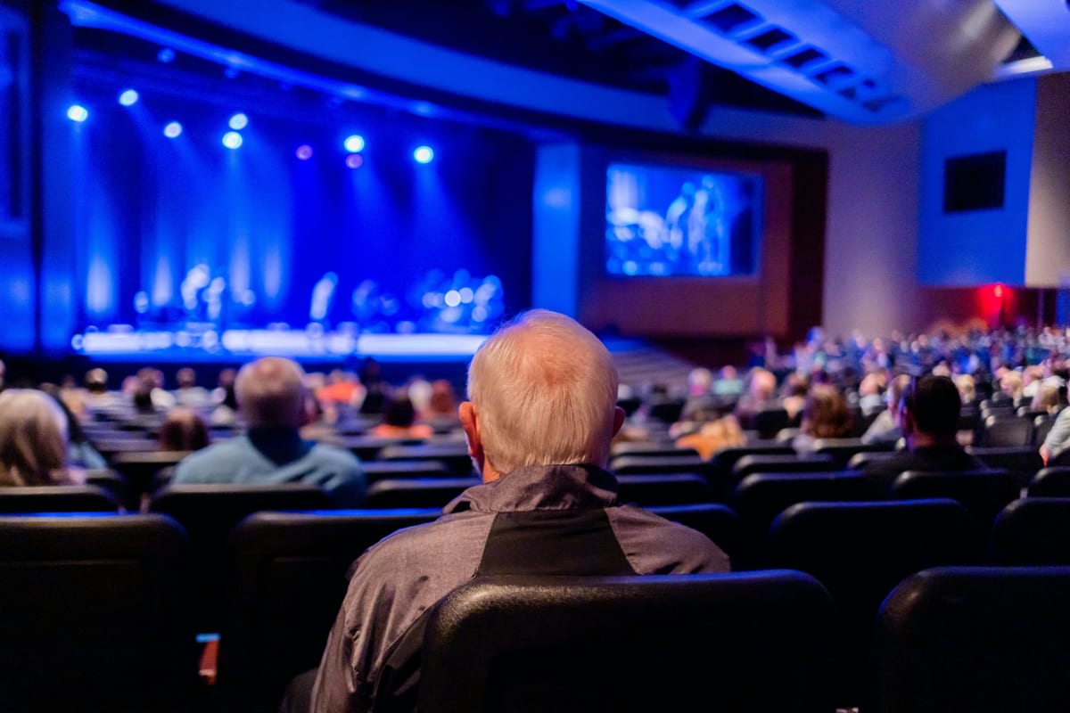 Audience seated in a hall facing a lit stage