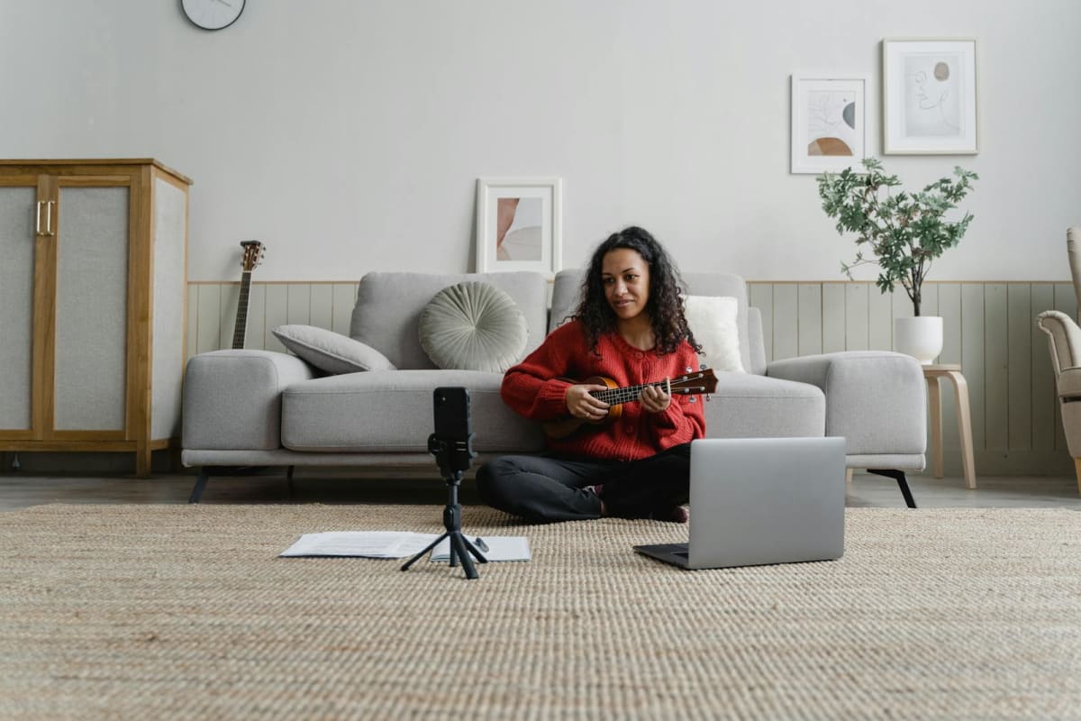 Musician filming a home performance with a phone, laptop, and microphone