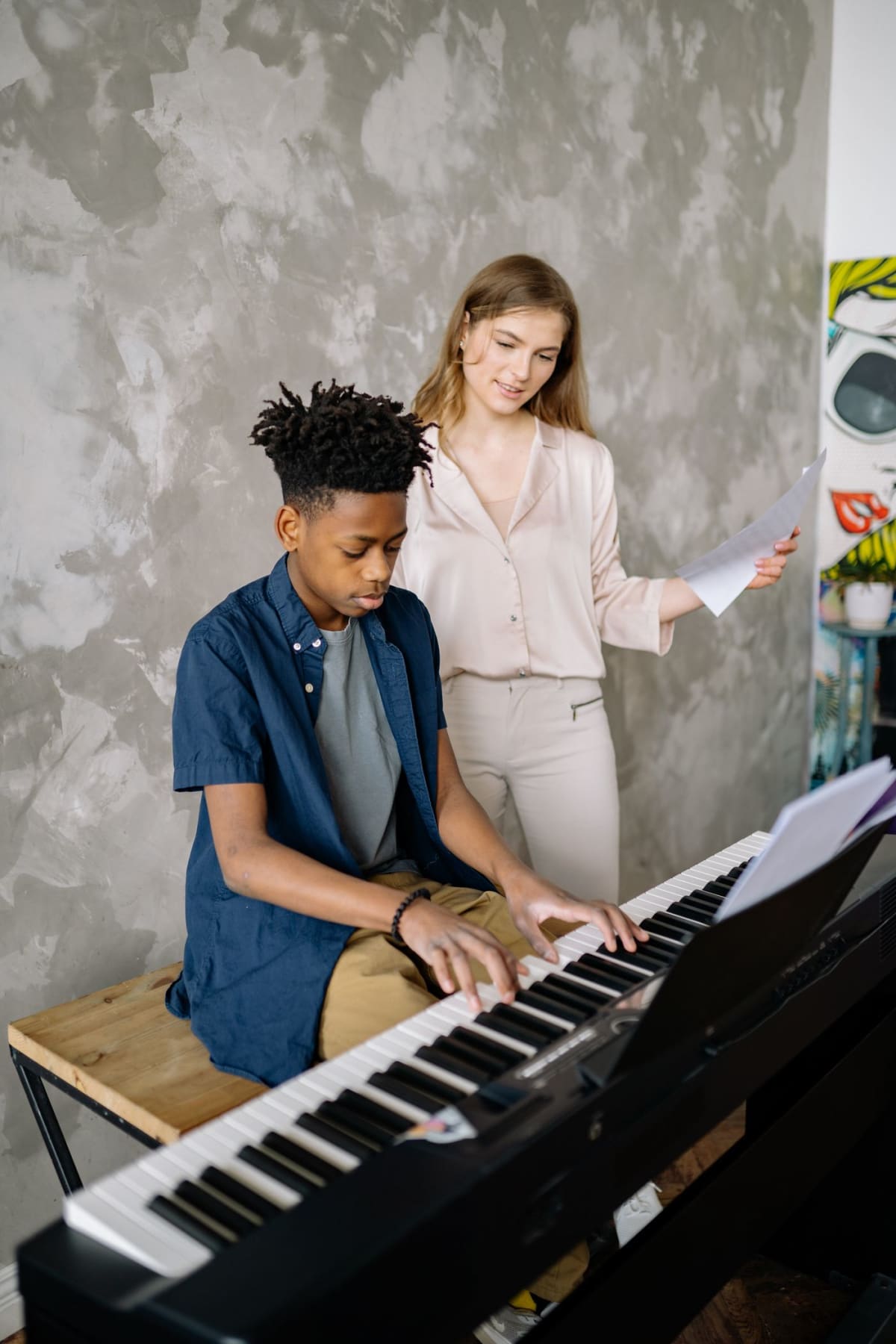 Student playing piano while a teacher sits nearby and observes