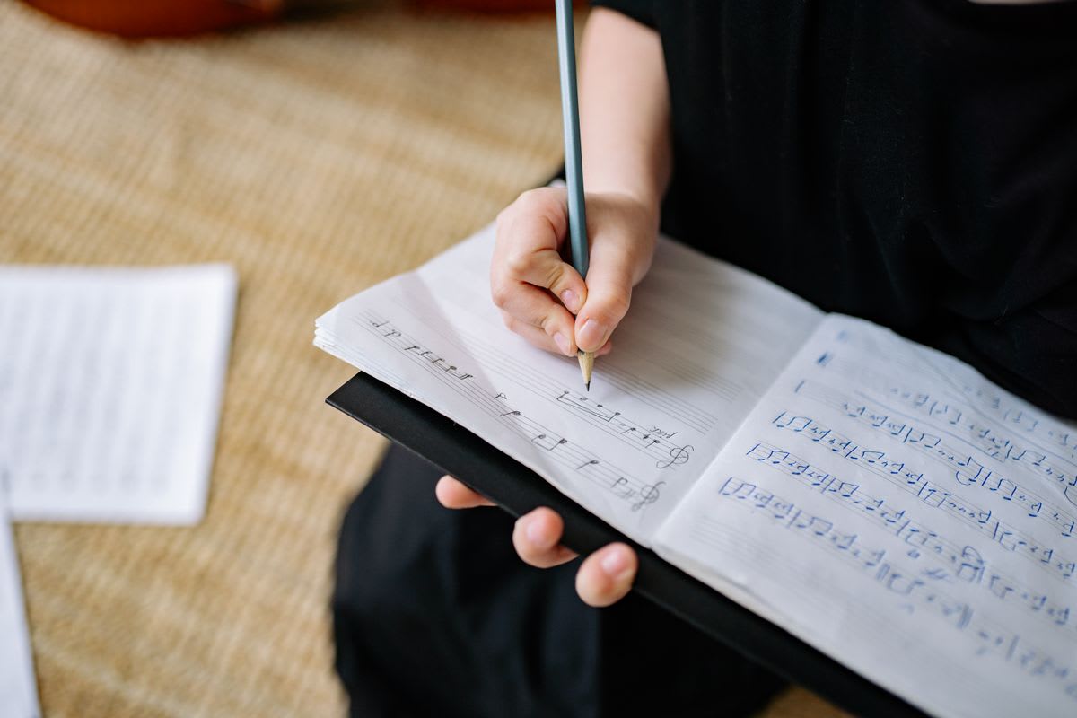 A musician's hand writing musical notes and reflections in a notebook