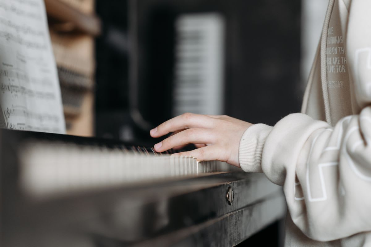A musician's hand on piano keys beside open sheet music