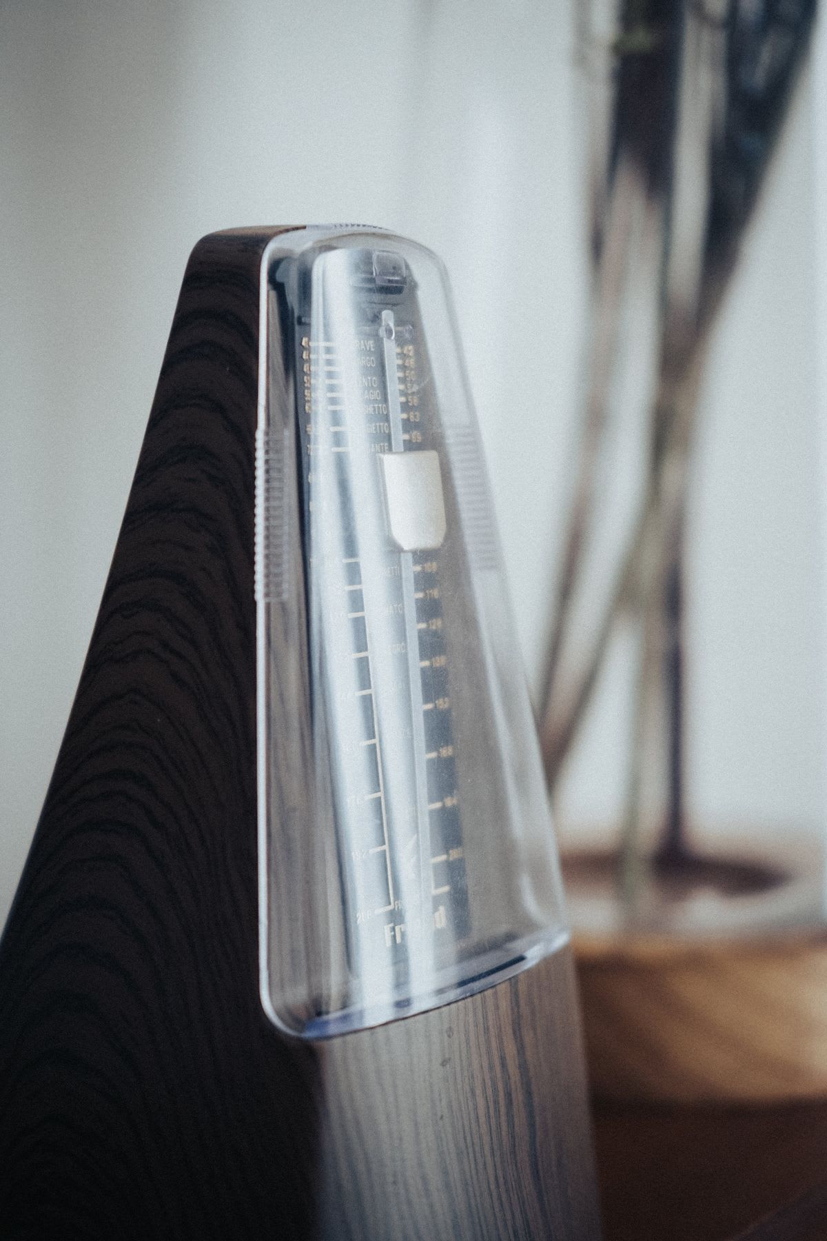 A close-up of a wooden metronome with its tempo scale visible