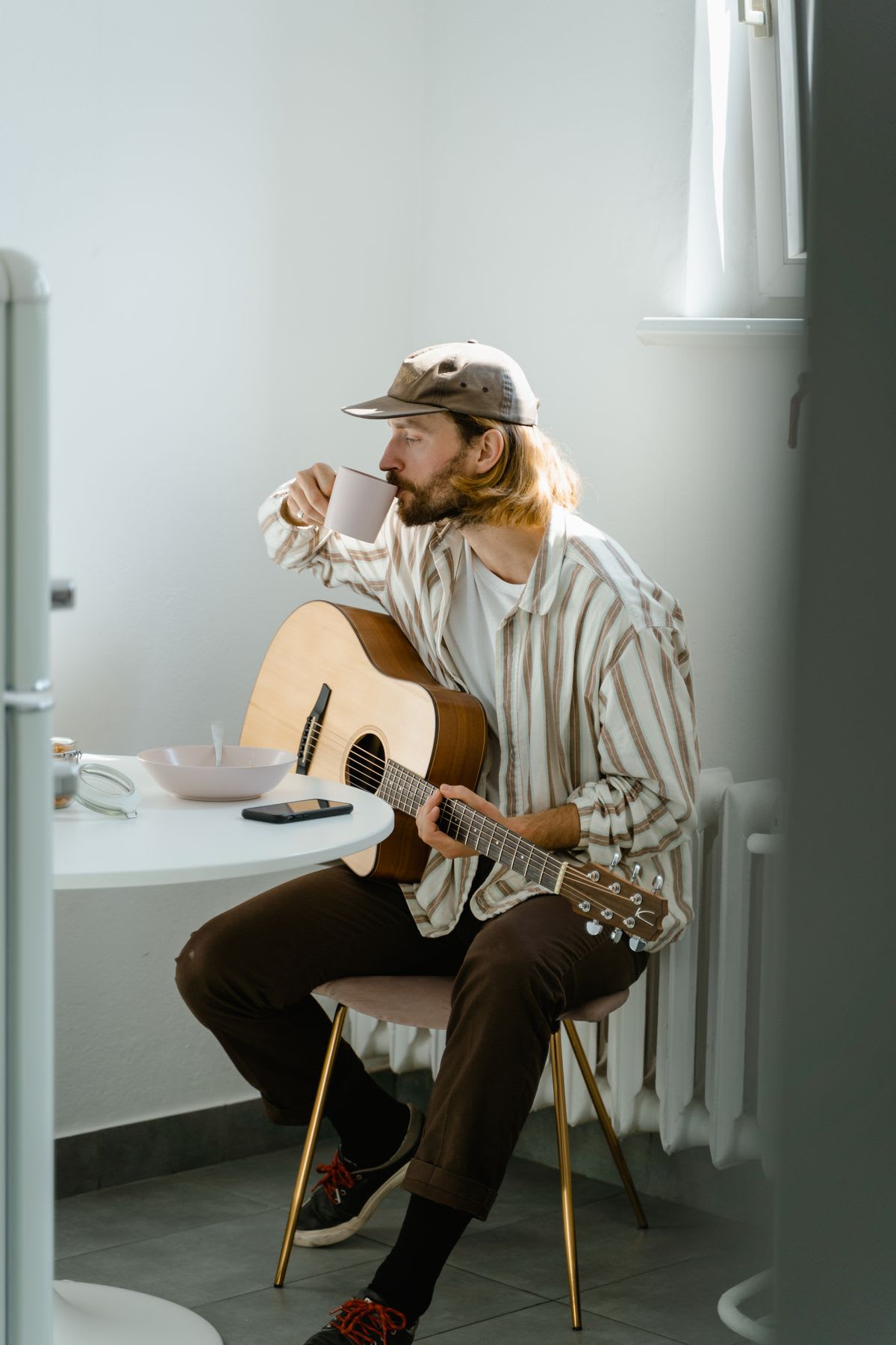 A relaxed musician sipping coffee with a guitar, phone resting on the table