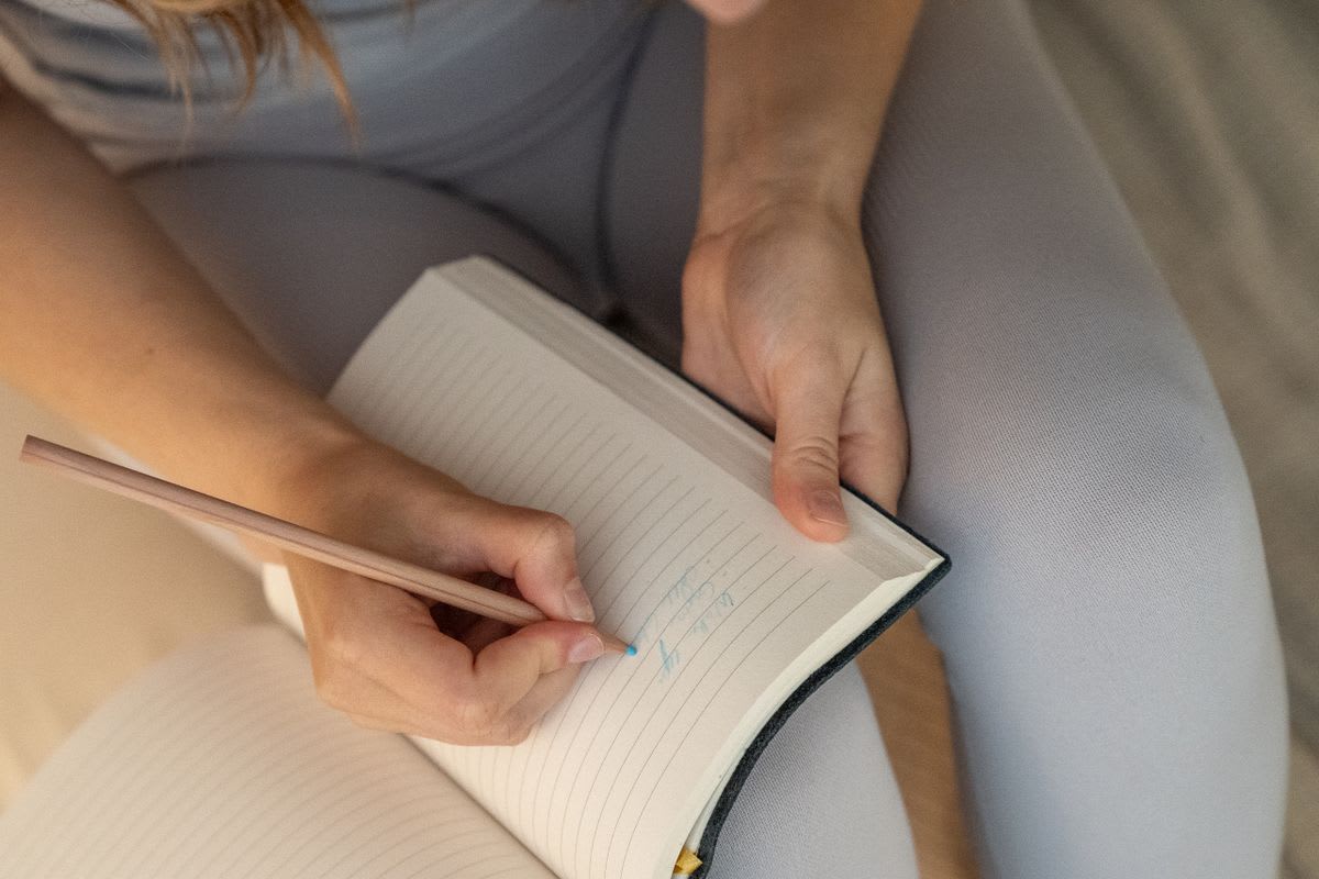 A person writing a short note in a small lined notebook with a pencil