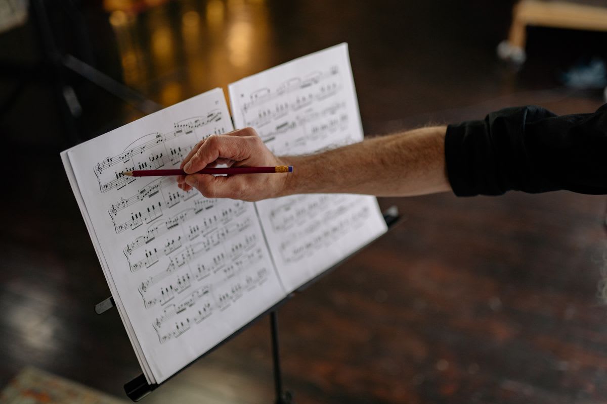 A hand marking a passage of sheet music on a stand with a pencil