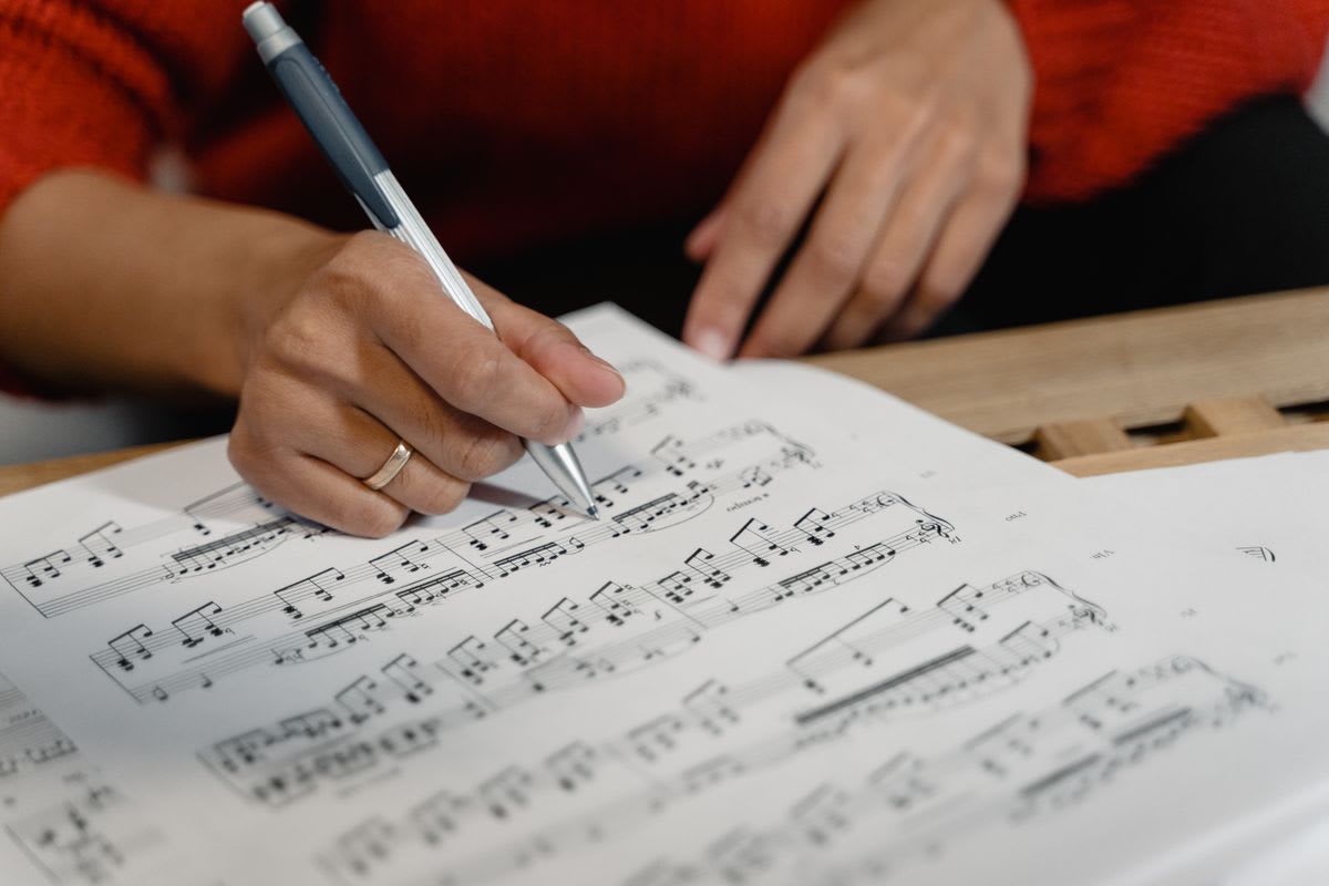 A musician's hands writing a short note on a sheet of music with a pen