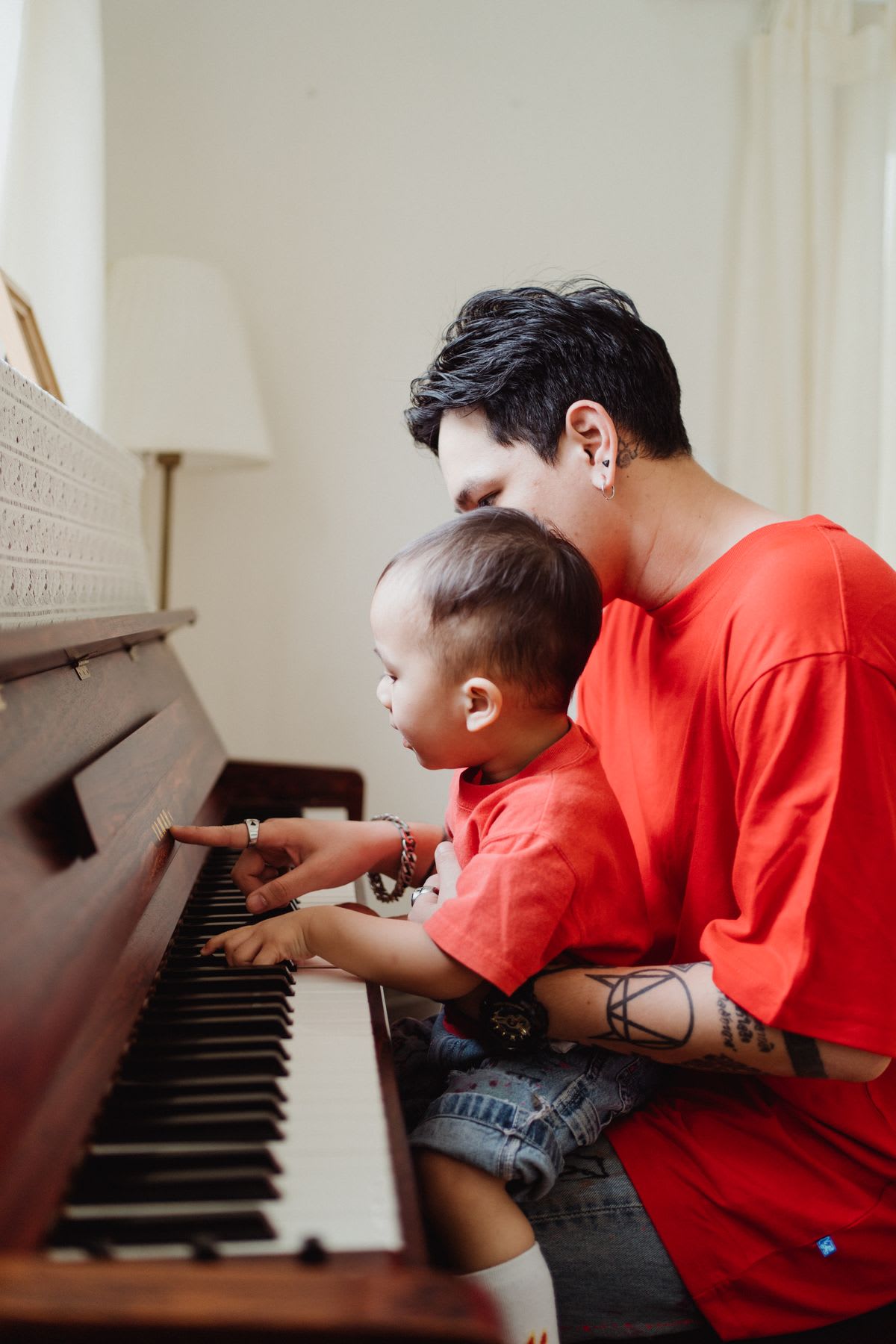 A parent and a young child playing an upright piano together at home