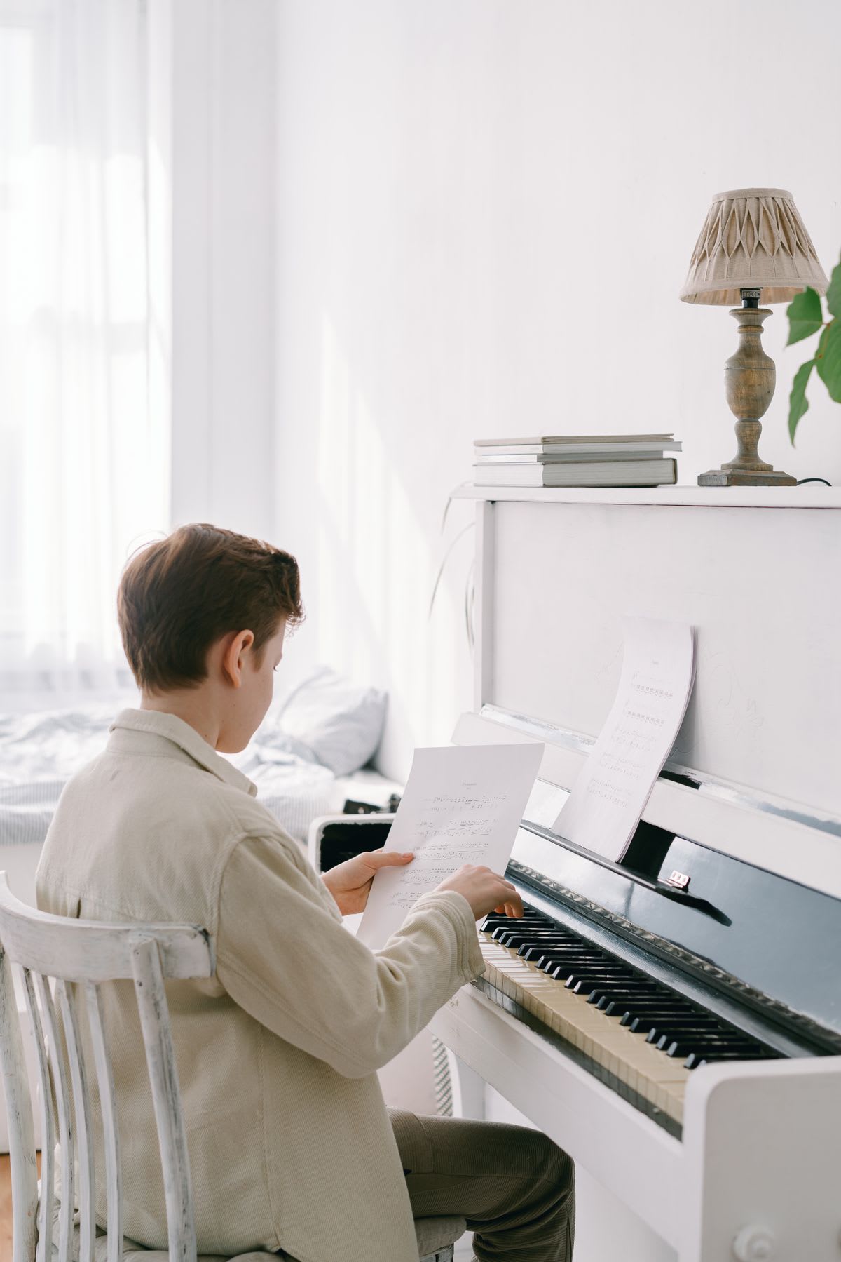 A young student practising alone at an upright piano in a bright bedroom