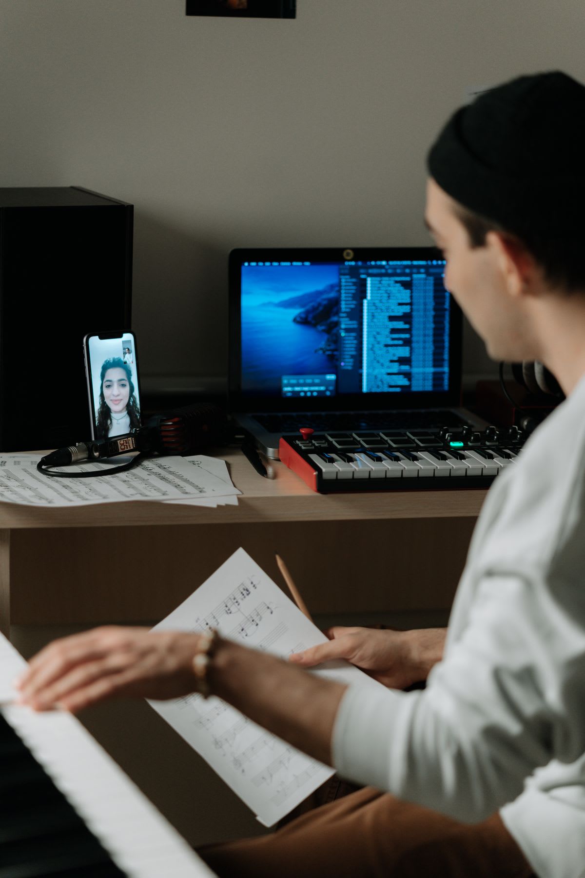 A student at the piano during an online lesson, teacher visible on a phone mounted at keyboard height