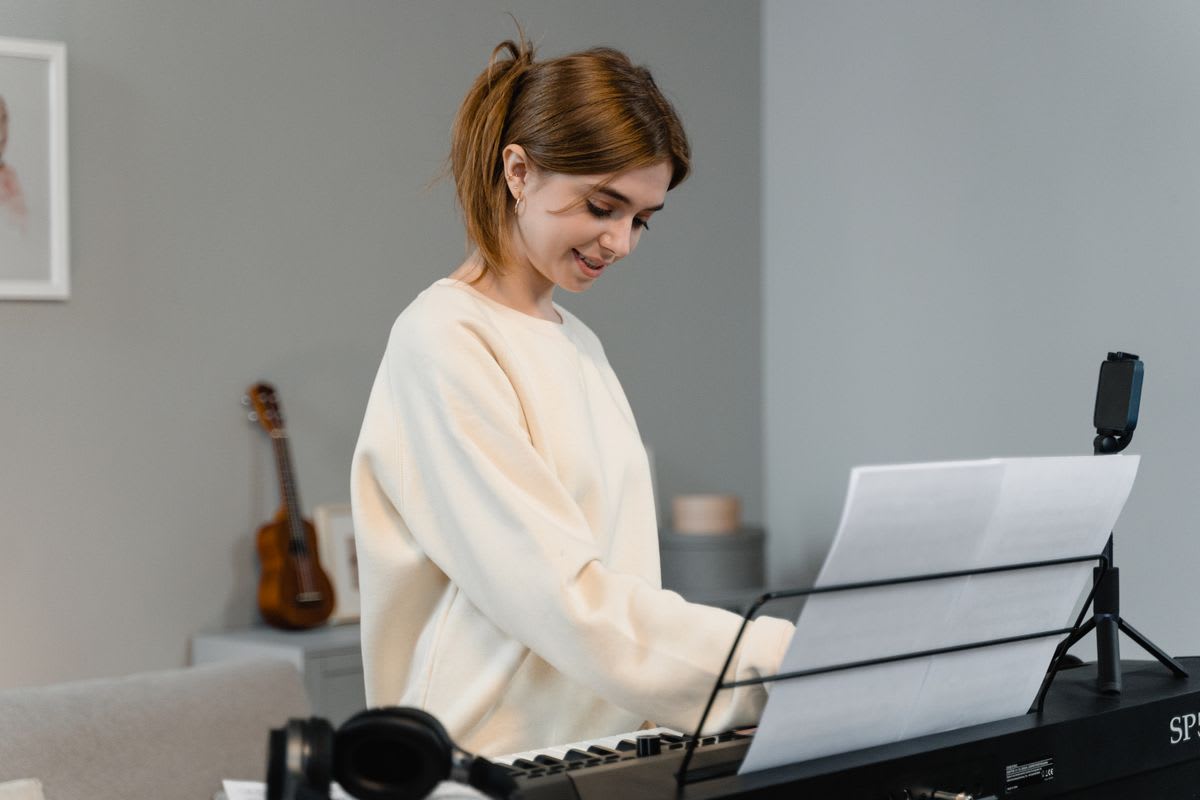 A smiling adult learner at a digital piano at home with a phone mounted for an online lesson