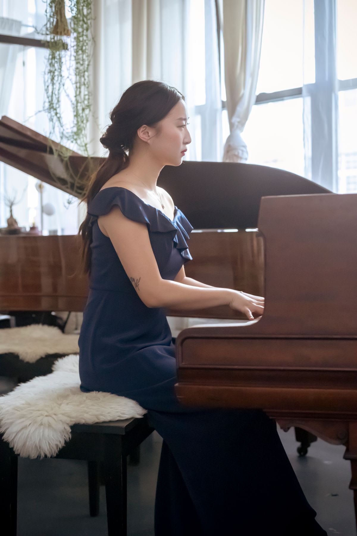 A young pianist in a formal dress playing a grand piano by a bright window