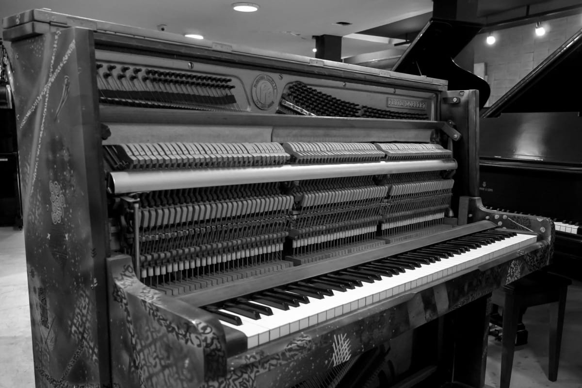 An upright acoustic piano with its hammers, action, strings, and keys exposed