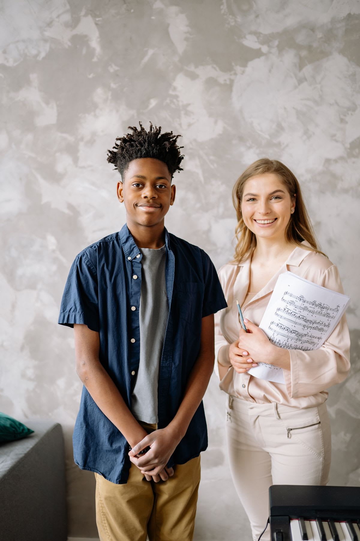 A music teacher and student standing beside a piano with their printed score