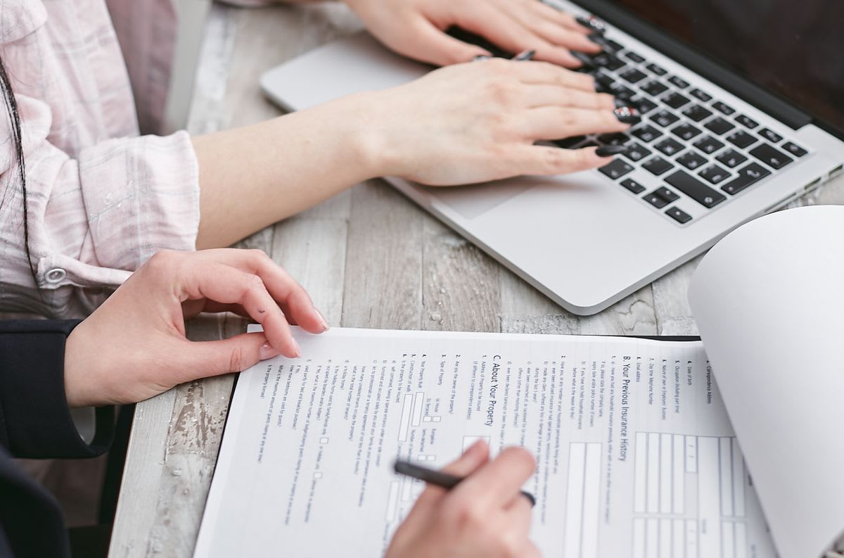 Two people carefully reviewing records and a form beside a laptop