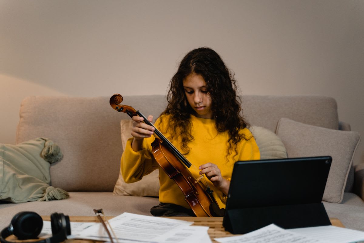 A violinist practices beside a tablet and printed sheet music