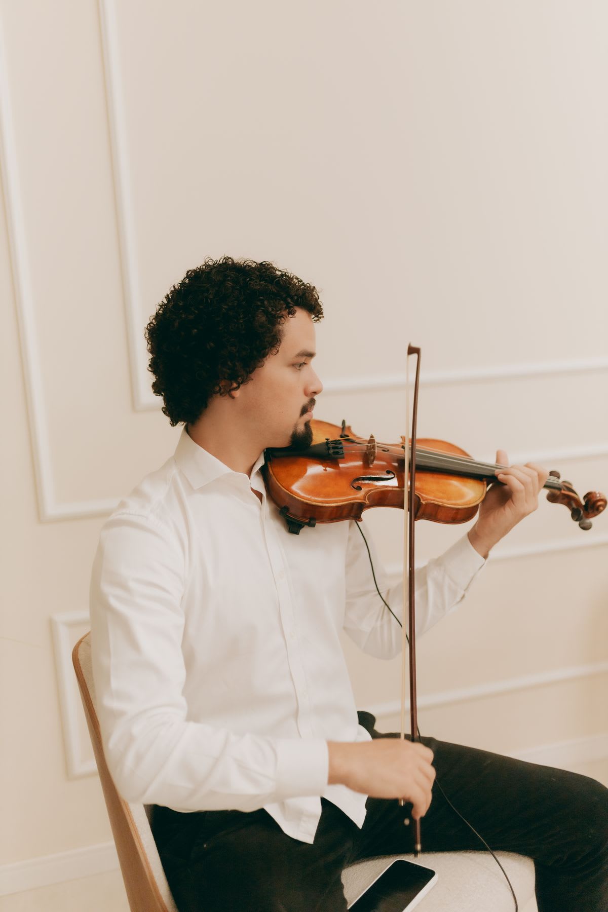 Um violinista pratica sentado com um telemóvel ao lado