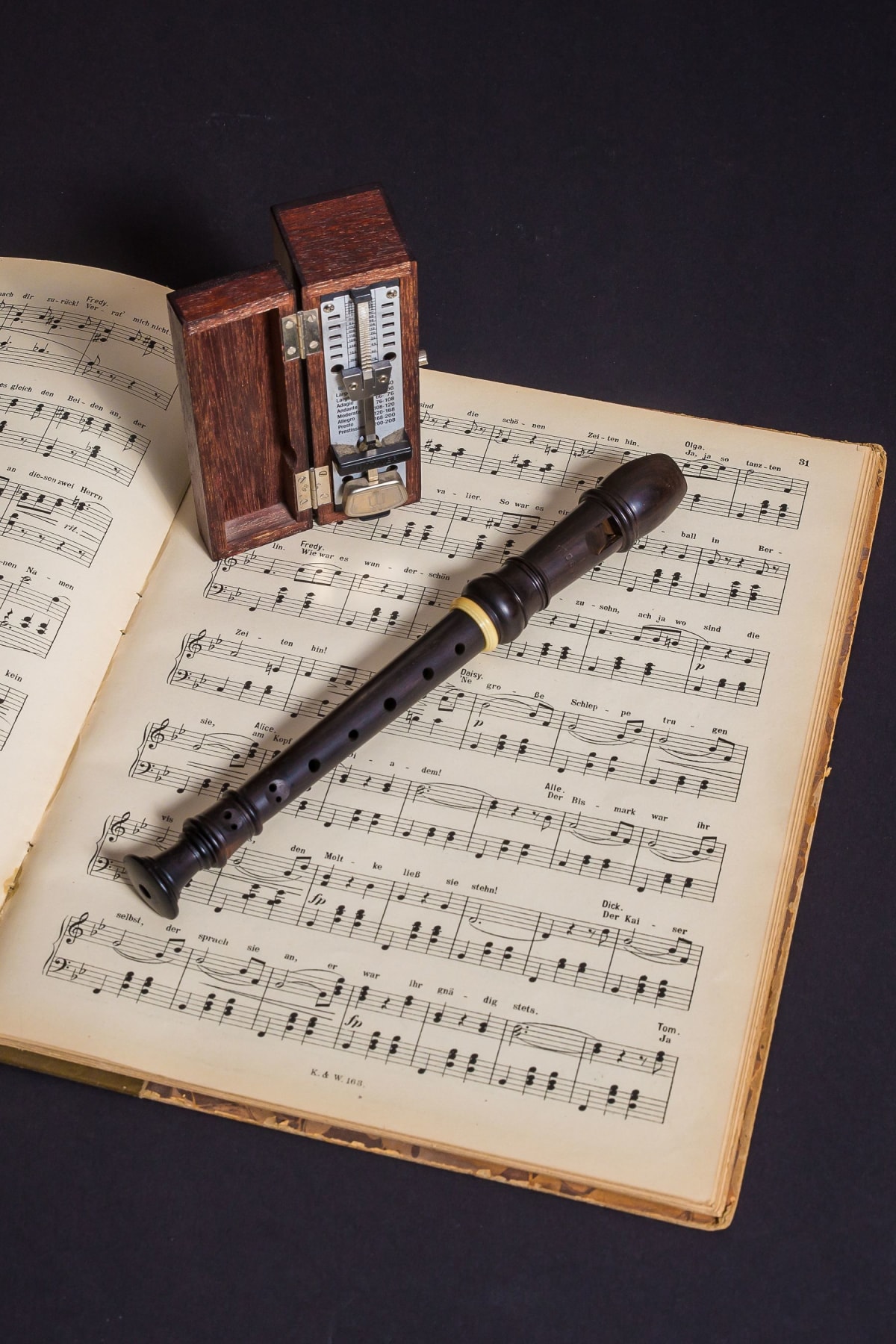 Pocket-size wooden mechanical metronome beside a recorder on open sheet music
