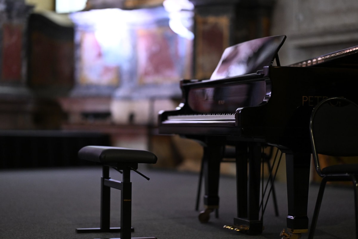 An adjustable black piano seat with a side lever beside a grand piano
