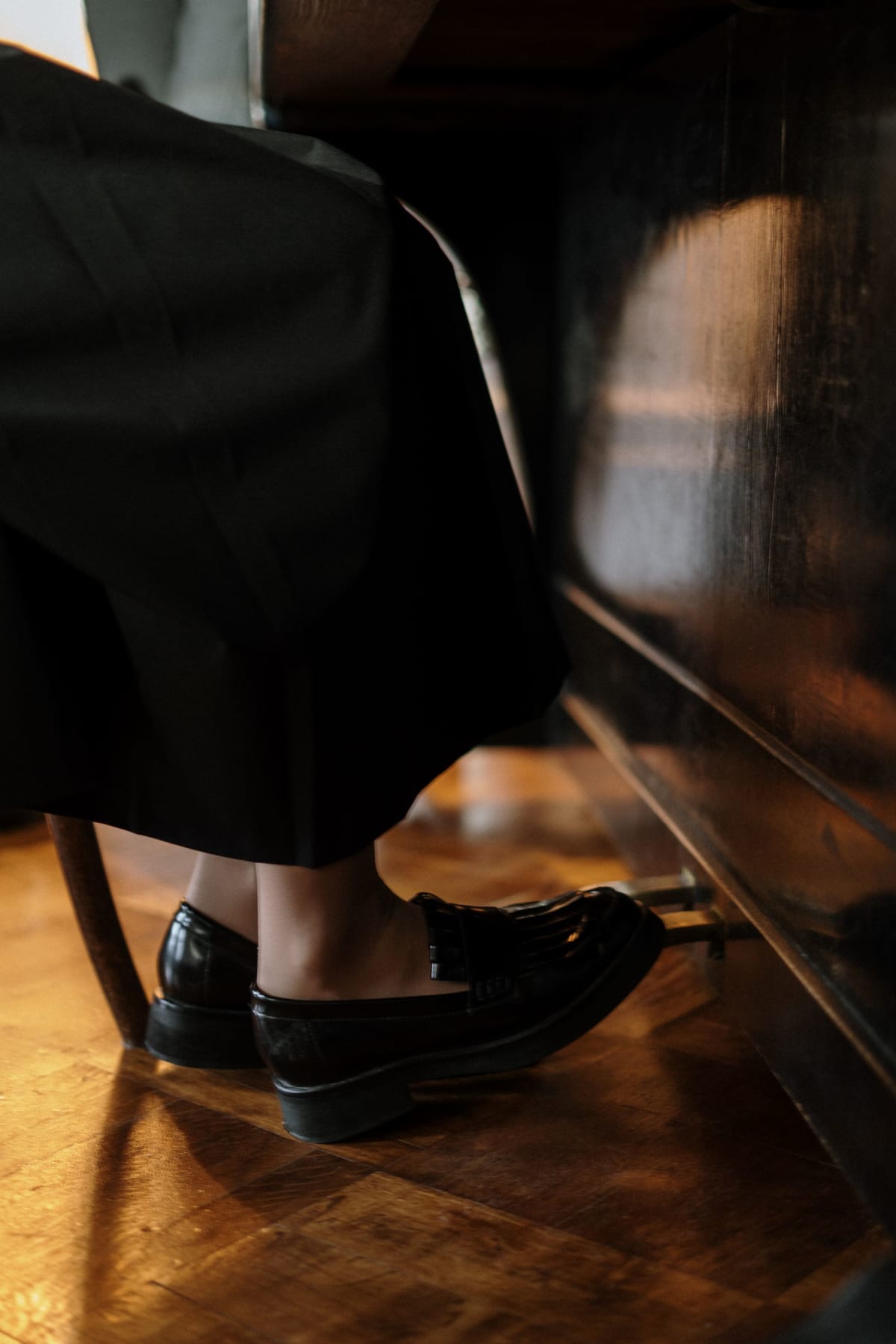 Seated pianist in black shoes using the pedals of an upright piano