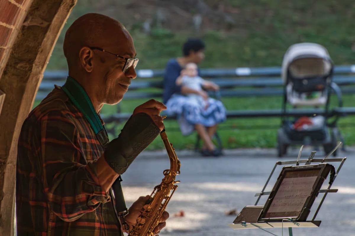 Saxophonist beside a lightweight folding music stand during an outdoor park performance