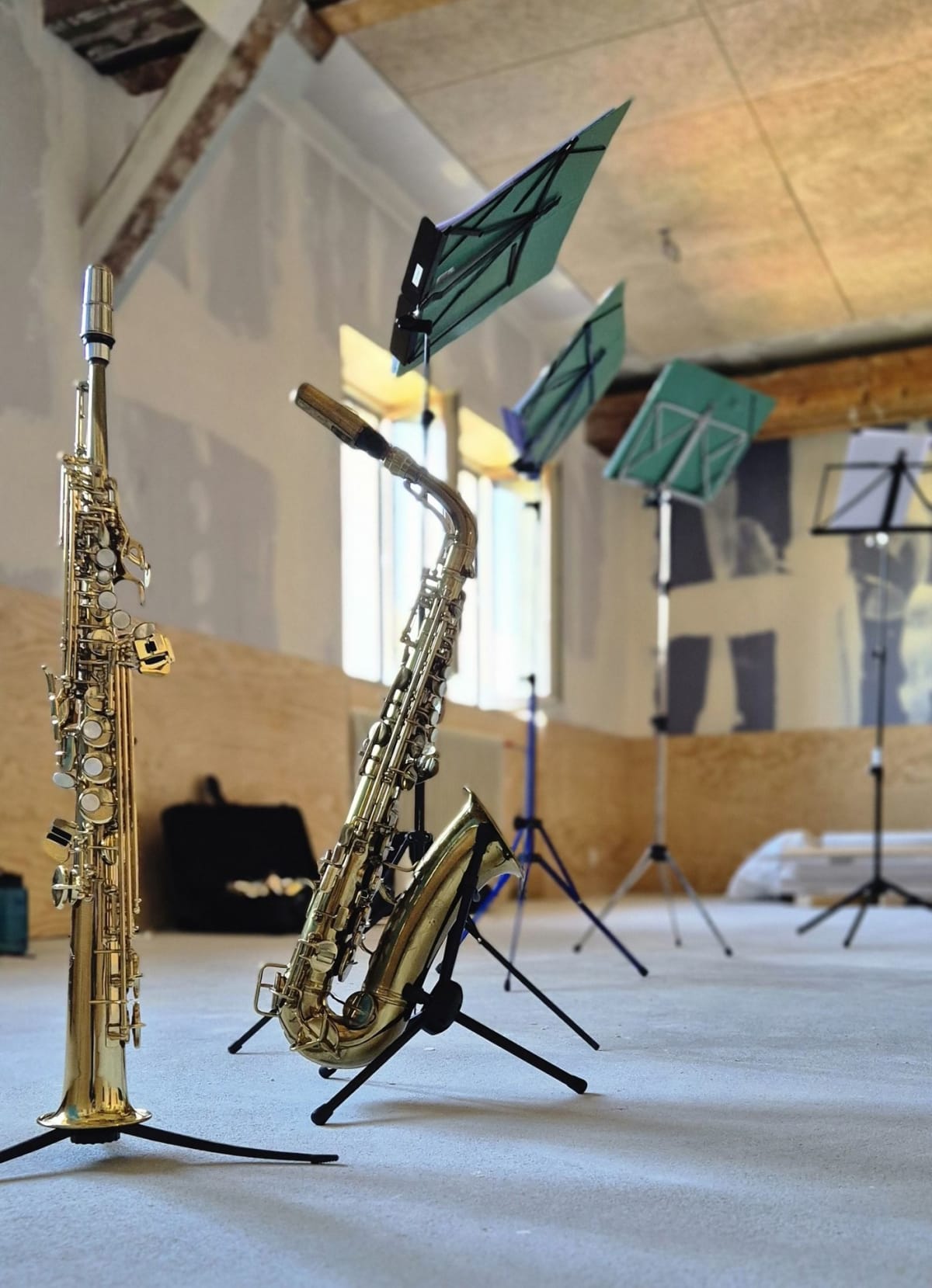 Saxophones and several lightweight tripod music stands set up in an empty rehearsal room