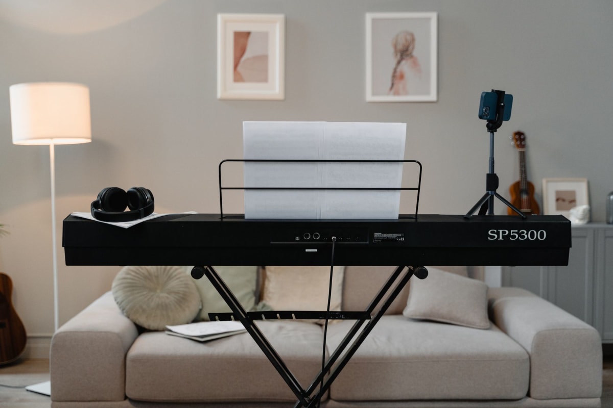 Black electronic piano on an X-stand with sheet music and headphones in a living room