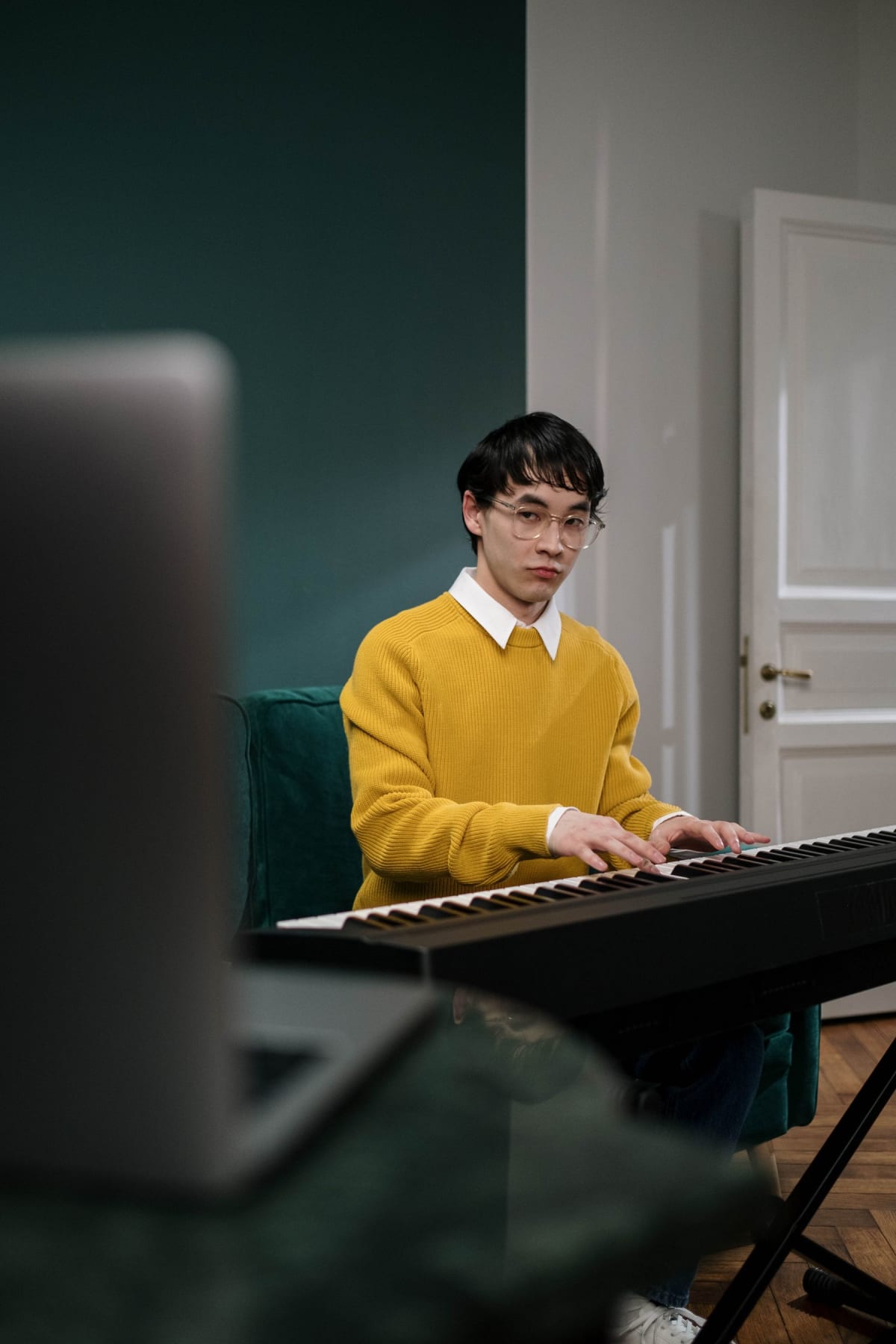 Pianist in a yellow sweater playing a slim electronic piano on an X-stand