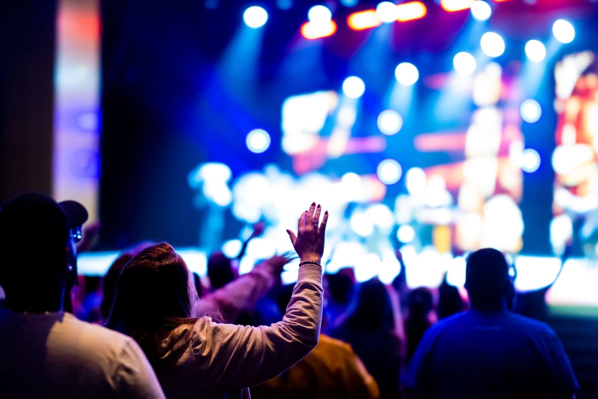 Concert audience facing a brightly lit stage with one hand raised