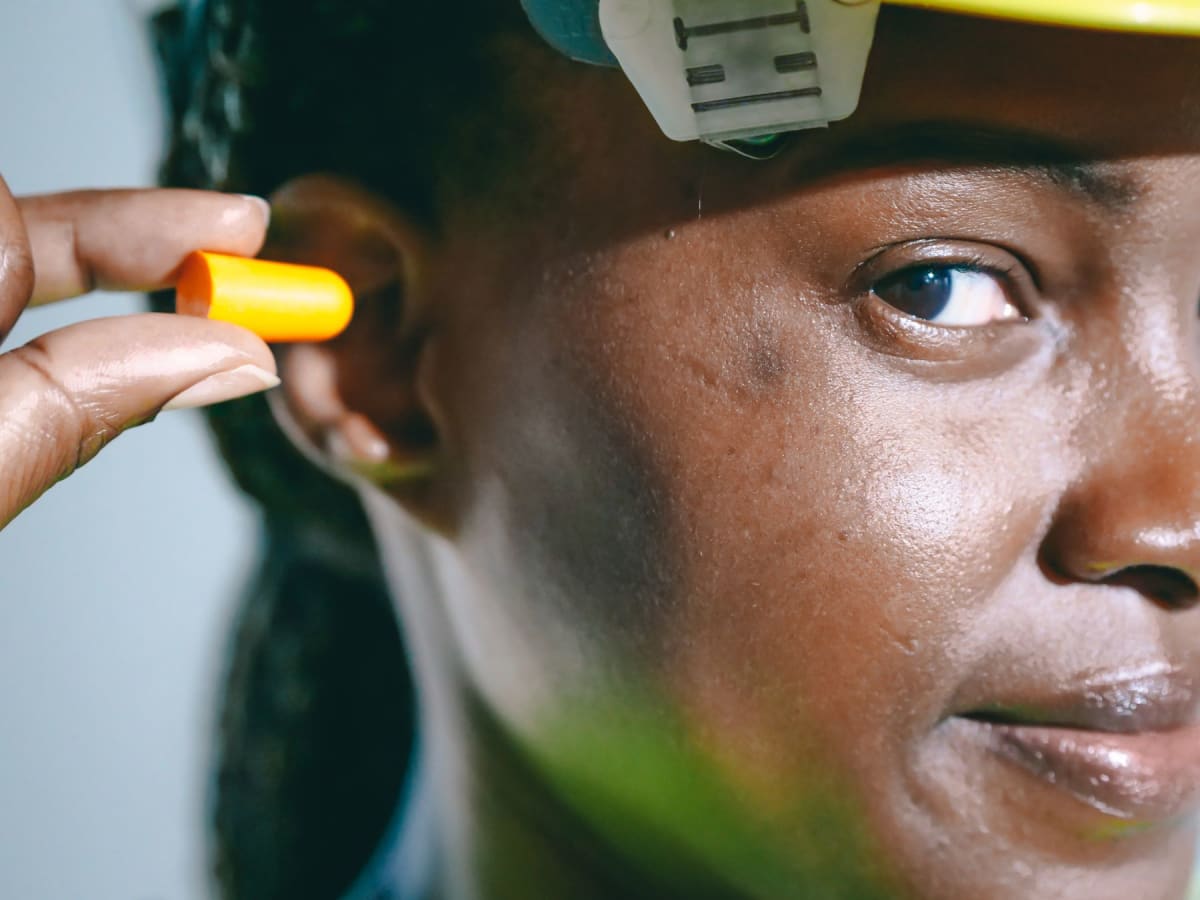 Person holding an orange foam earplug beside their ear