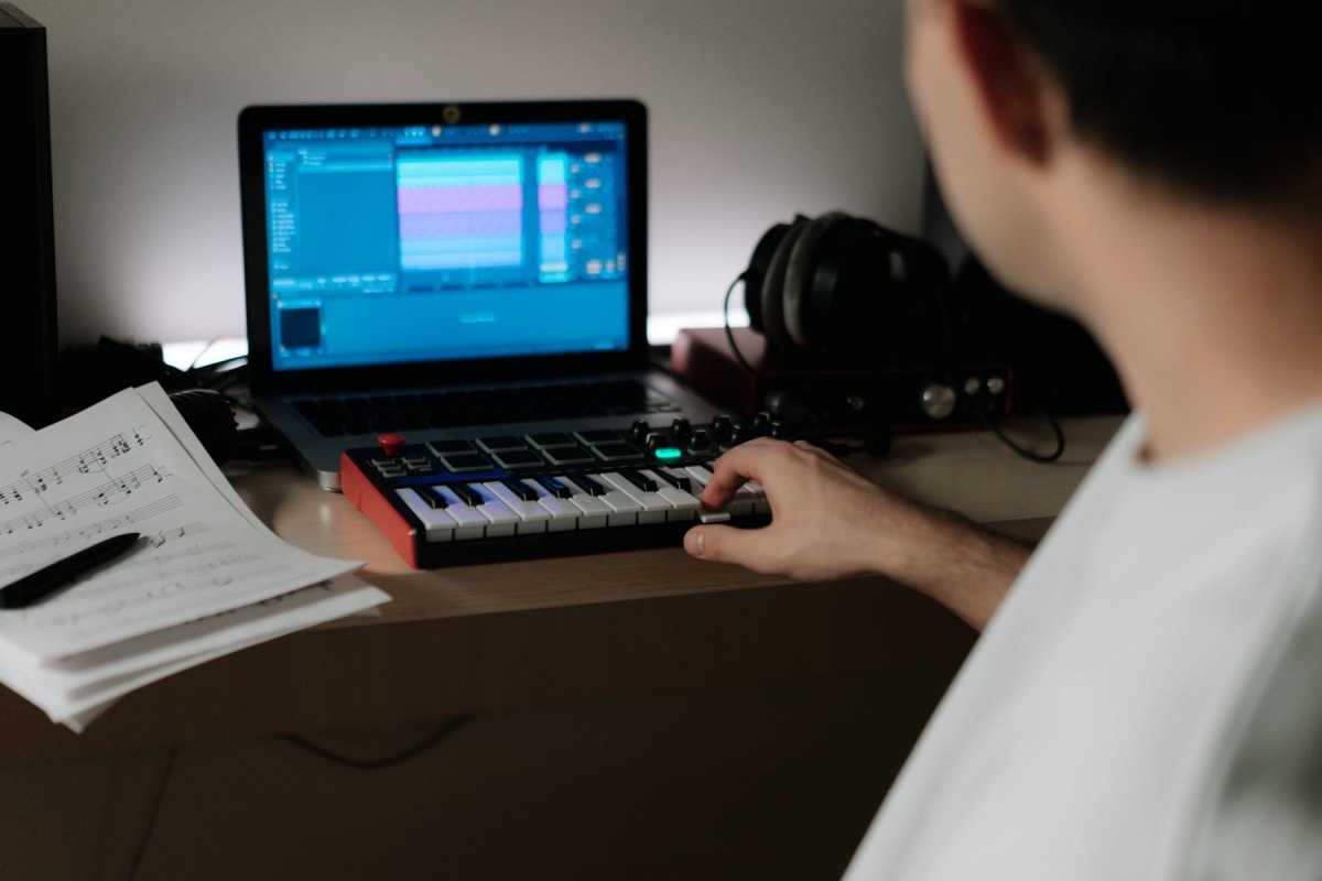 Musician playing a compact MIDI keyboard beside a laptop and sheet music